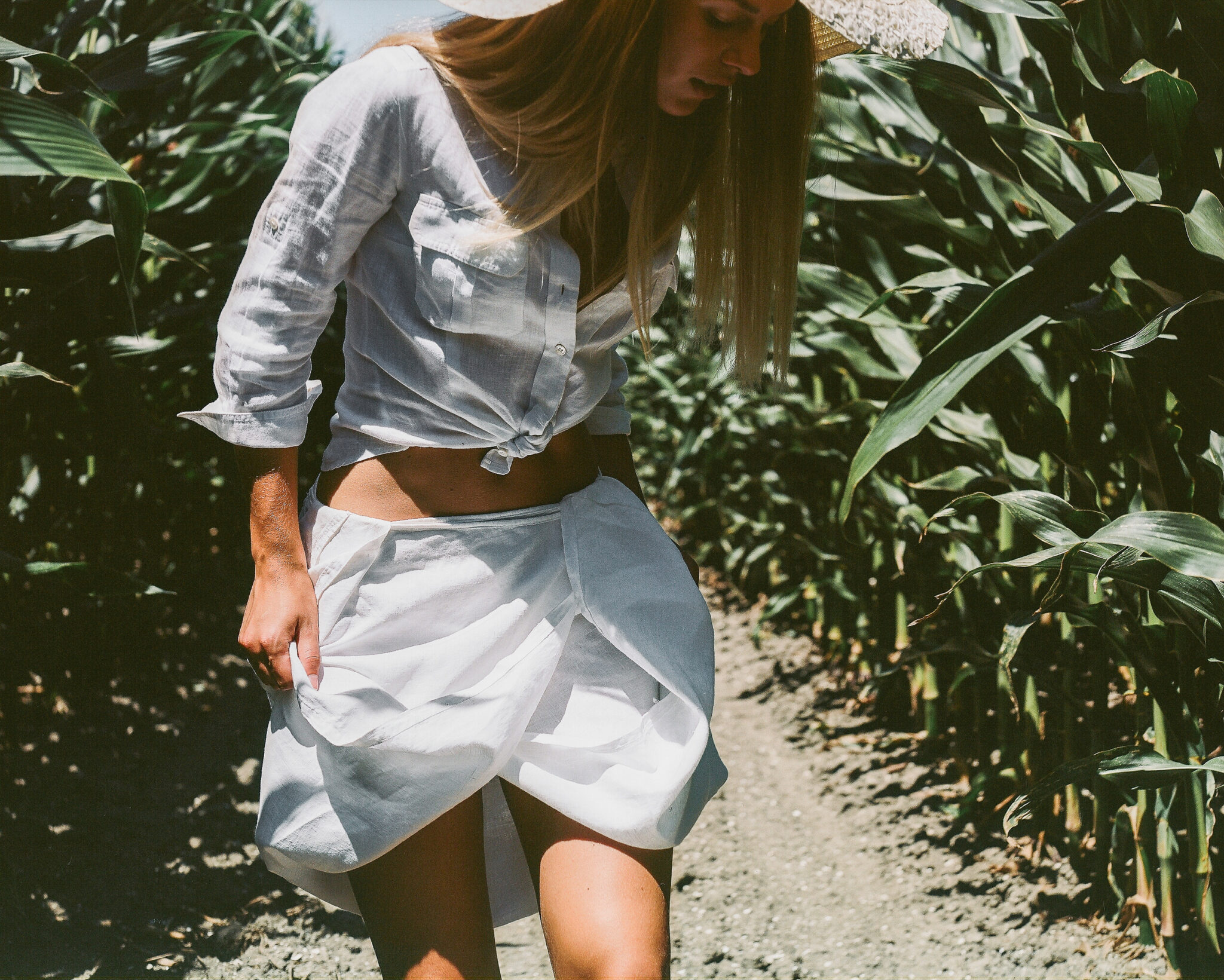 Modella con camicia bianca annodata e gonna raccolta in mezzo a un campo di pannocchie, fotografia analogica con Mamiya RZ67