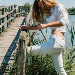 Modella con camicia bianca annodata e jeans bianchi su un ponte, fotografia analogica