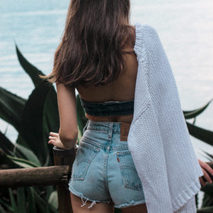Modella di spalle con top e shorts di jeans, con maglioncino bianco, guarda verso il lago di Como