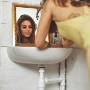Modella con vestito giallo, appoggiata ad un lavandino, si guarda allo specchio, fotografia analogica con Mamiya RZ67 medio formato