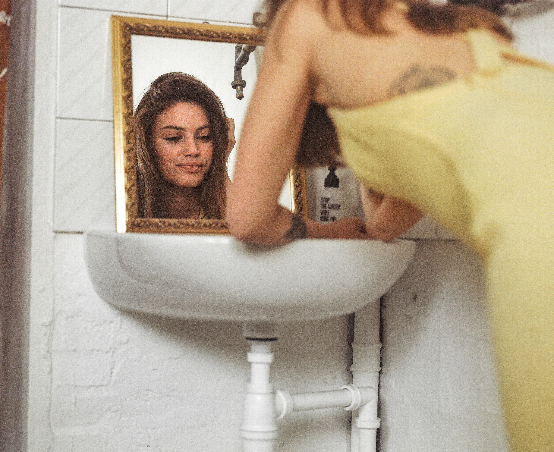Modella con vestito giallo, appoggiata ad un lavandino, si guarda allo specchio, fotografia analogica con Mamiya RZ67 medio formato